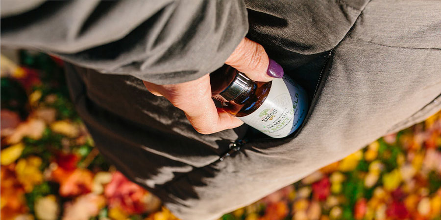 close up view of a person's hand holding a bottle of CBD soft gels and placing it into their bag